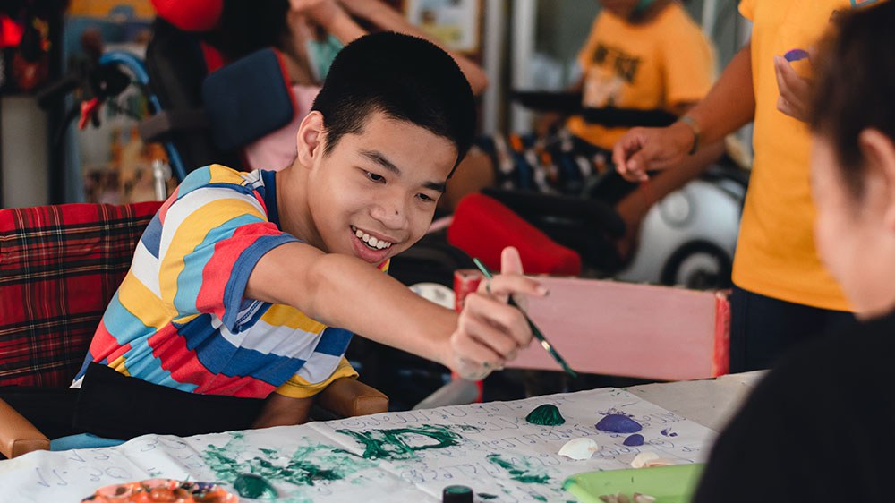 Ein Teenager mit Behinderung malt mit seinen Kamerad:innen