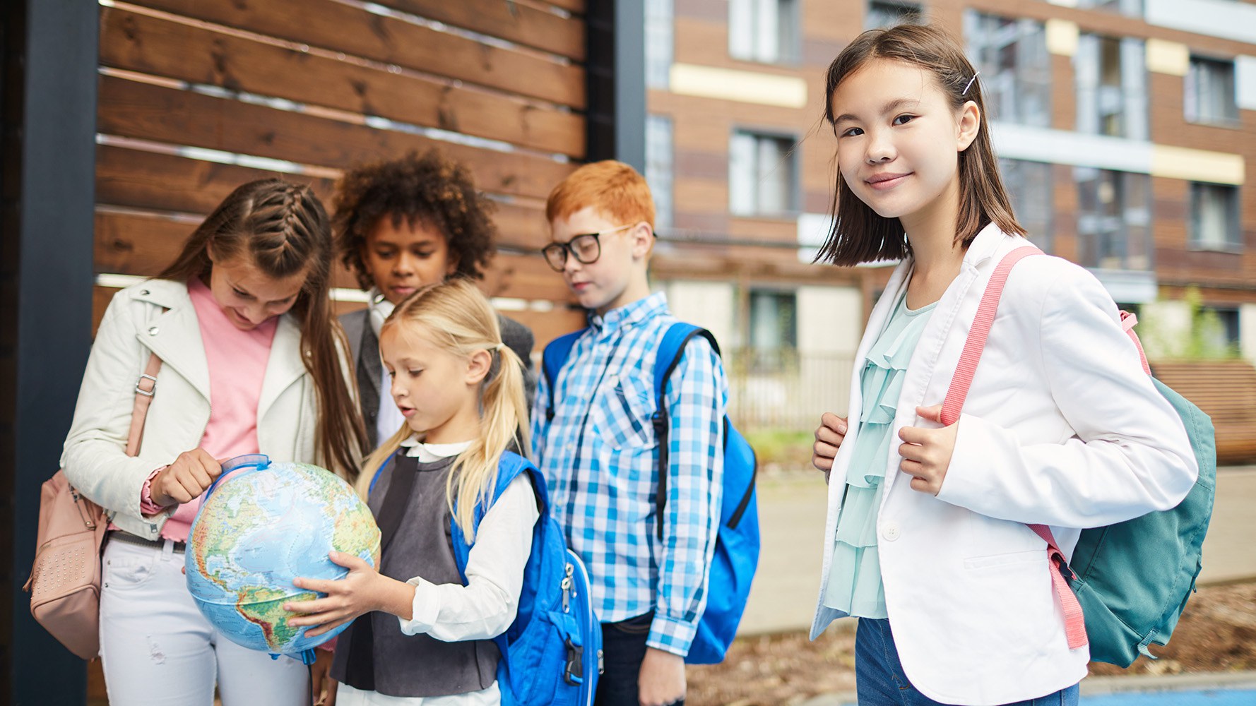 Vier Kinder schauen sich einen Globus an, im Vordergrund steht ein fünftes Mädchen und schaut in die Kamera