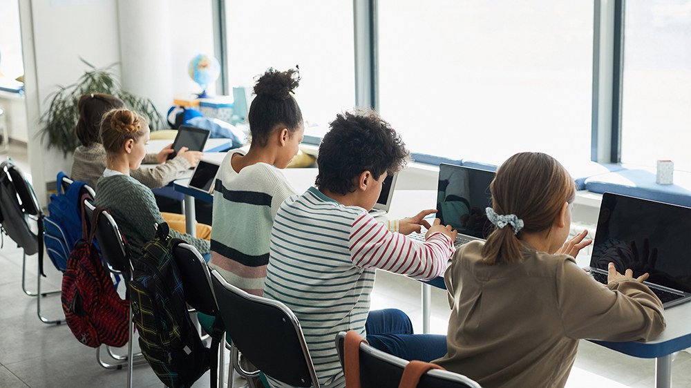 Blick von hinten auf fünf Kinder, die am Laptop arbeiten