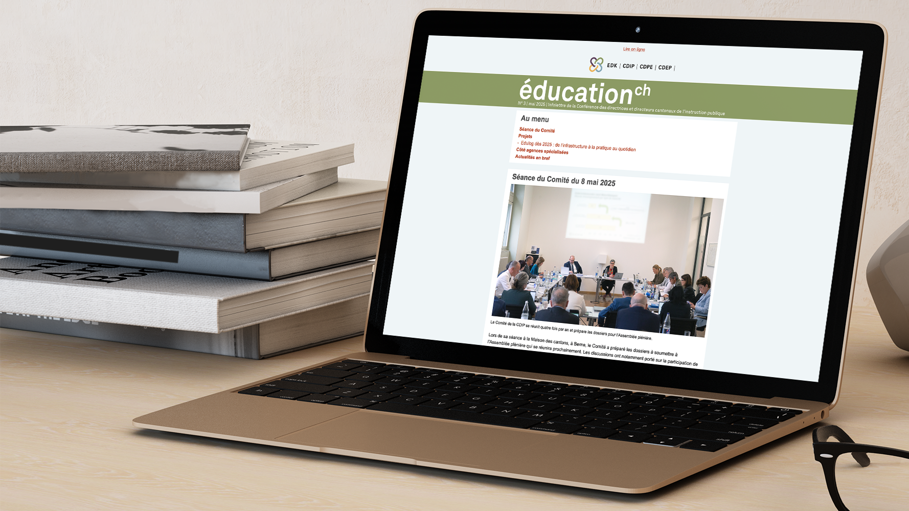 Laptop ouvert, montrant l’infolettre de la CDIP sur son écran; pile de livres posée à gauche du laptop